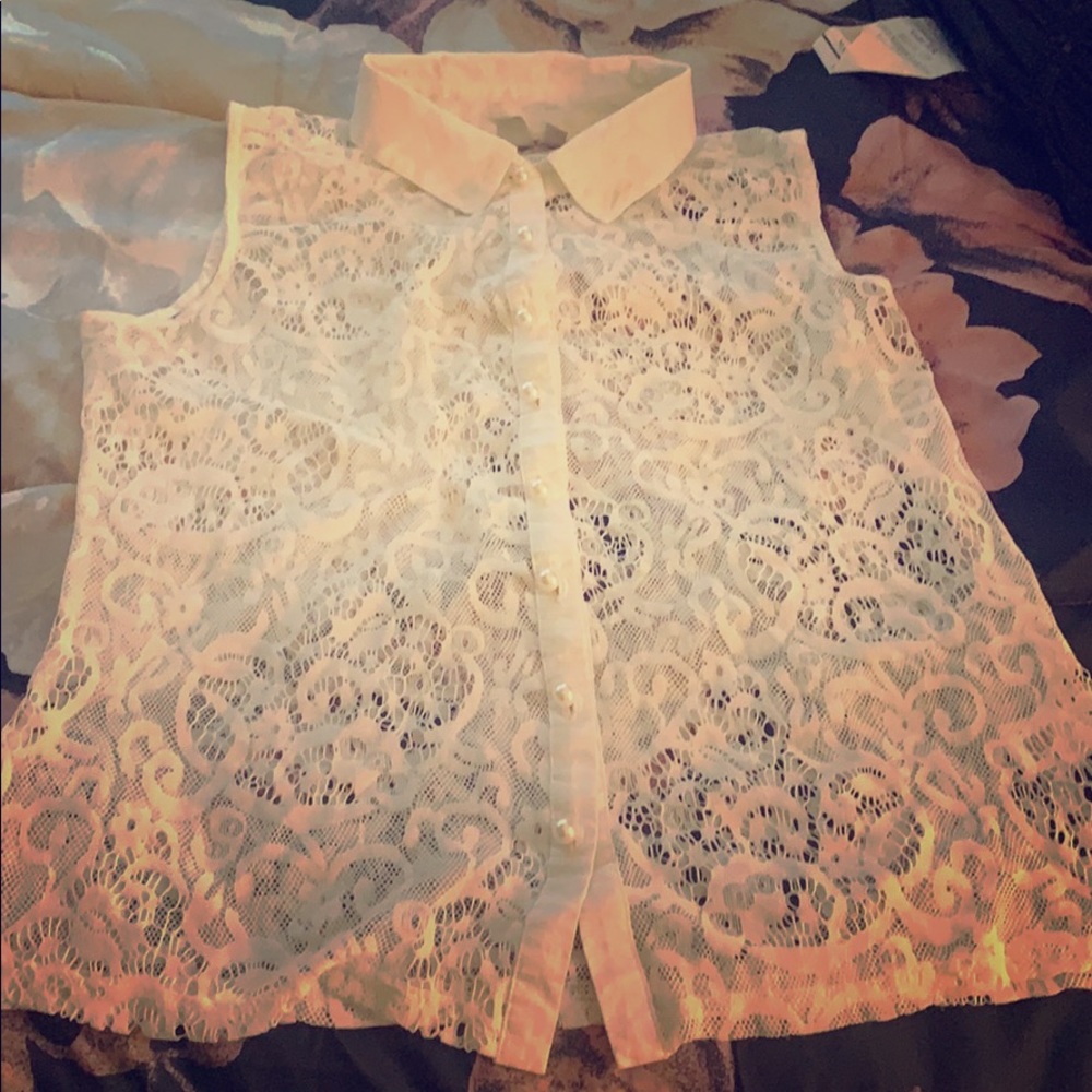 A white sleeveless button up shirt made of lace.